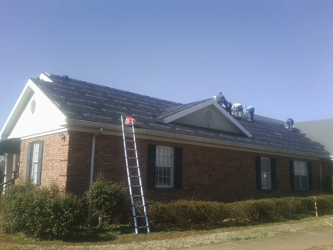 Crew tearing shingles off a brick ranch roof with a ladder set — Metal Roof Repair work by our crew in Jackson