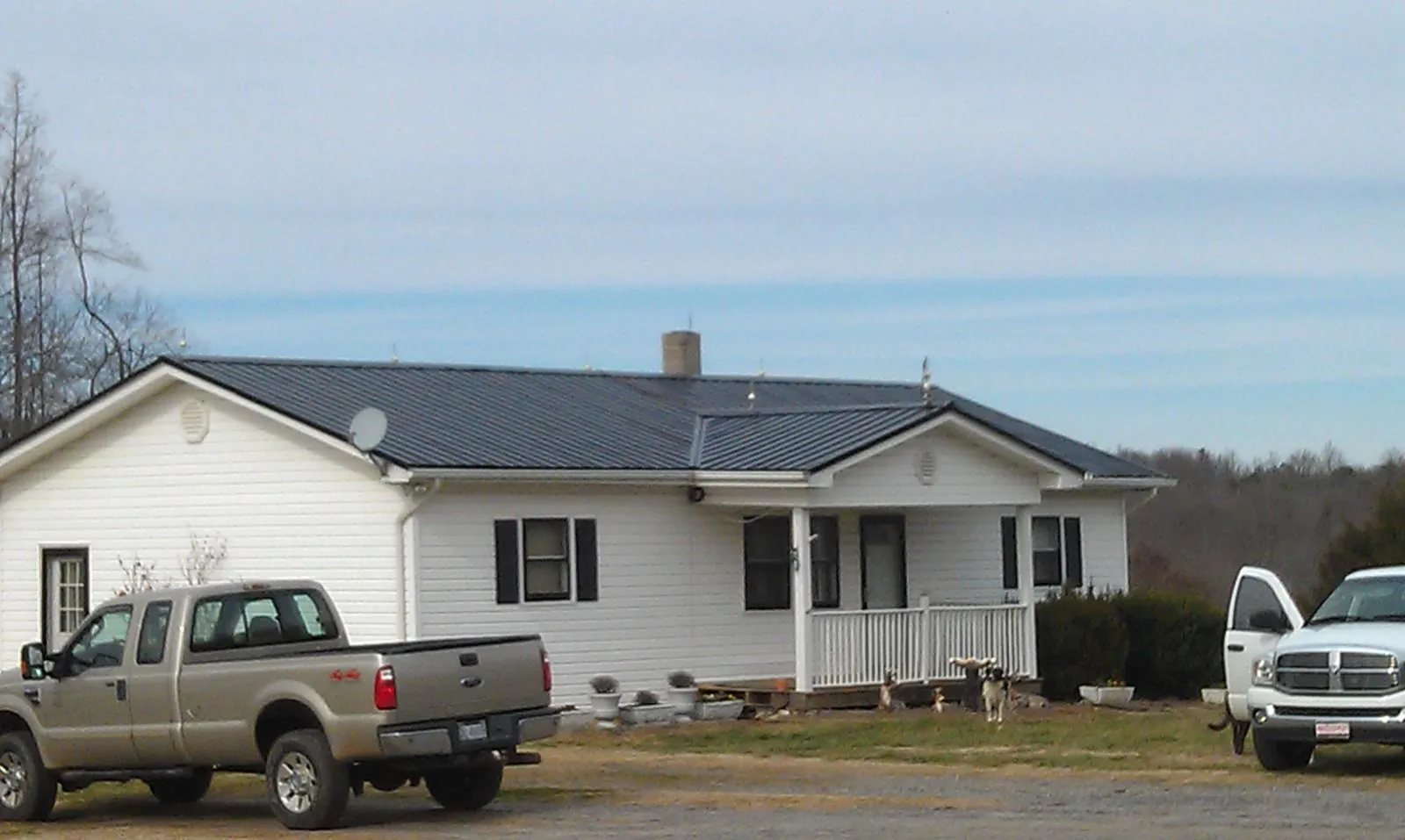 Finished dark metal roof on a white ranch home with work trucks parked in Jackson